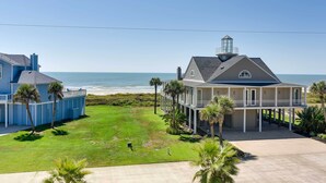 A beachfront property with a large house featuring a balcony and a lighthouse structure.