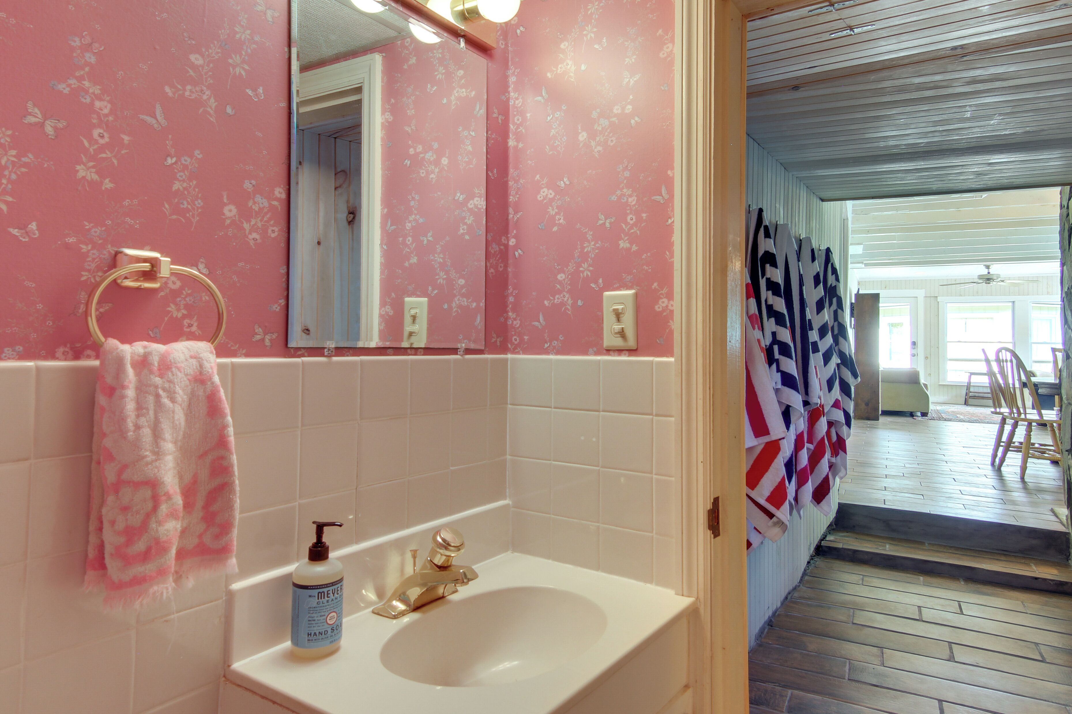 A bathroom with a white sink, a mirror, and a pink floral wallpaper.
