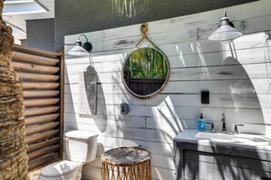 A bathroom with a white sink, two wall-mounted lights, a round mirror, and a toilet. - Luxury St. Petersburg Home w/ Pool + Bay Access! (St. Petersburg)