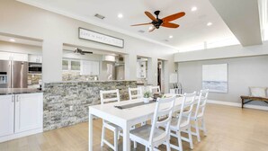 A spacious kitchen with white cabinetry, a stone island, and a dining area with white chairs.