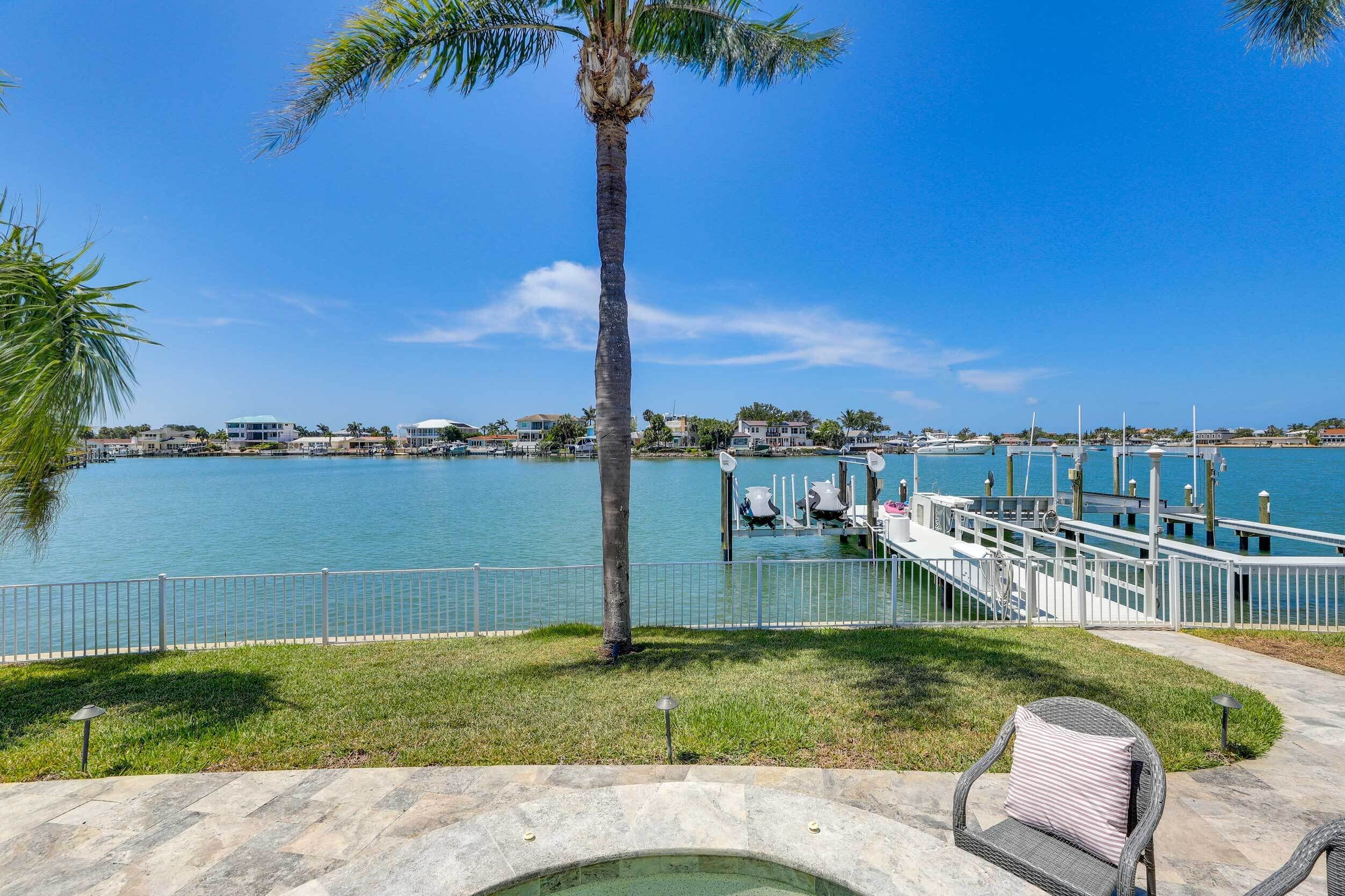 A waterfront property with a dock, a palm tree, and a chair by a pool.