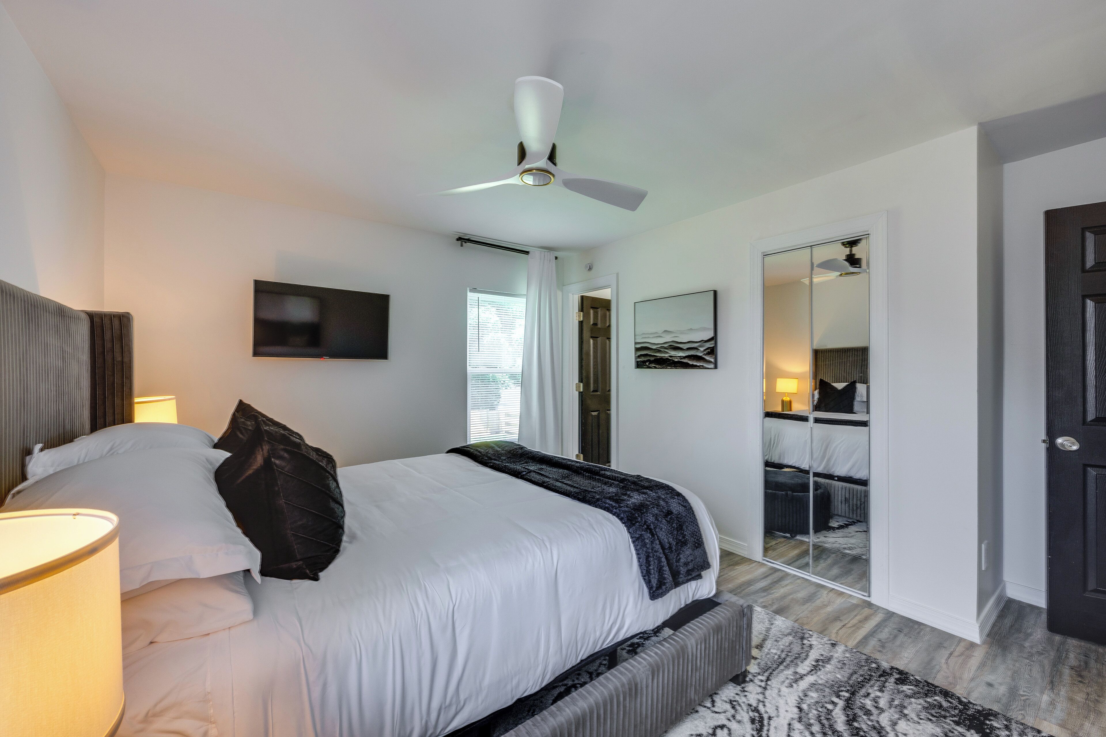 A modern bedroom with a large bed, a ceiling fan, a TV, a mirror, and a wardrobe.