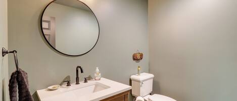 A bathroom with a round mirror, a white sink, a wooden cabinet, a toilet, and a towel hanging on a rack.