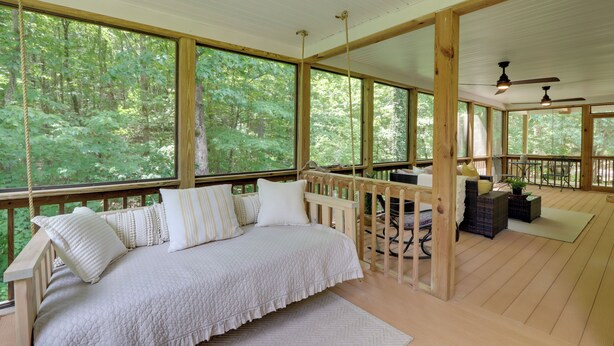 Ruime slaapkamer met een groot bed, houten hoofdeinde en uitzicht op een bos door grote ramen.
