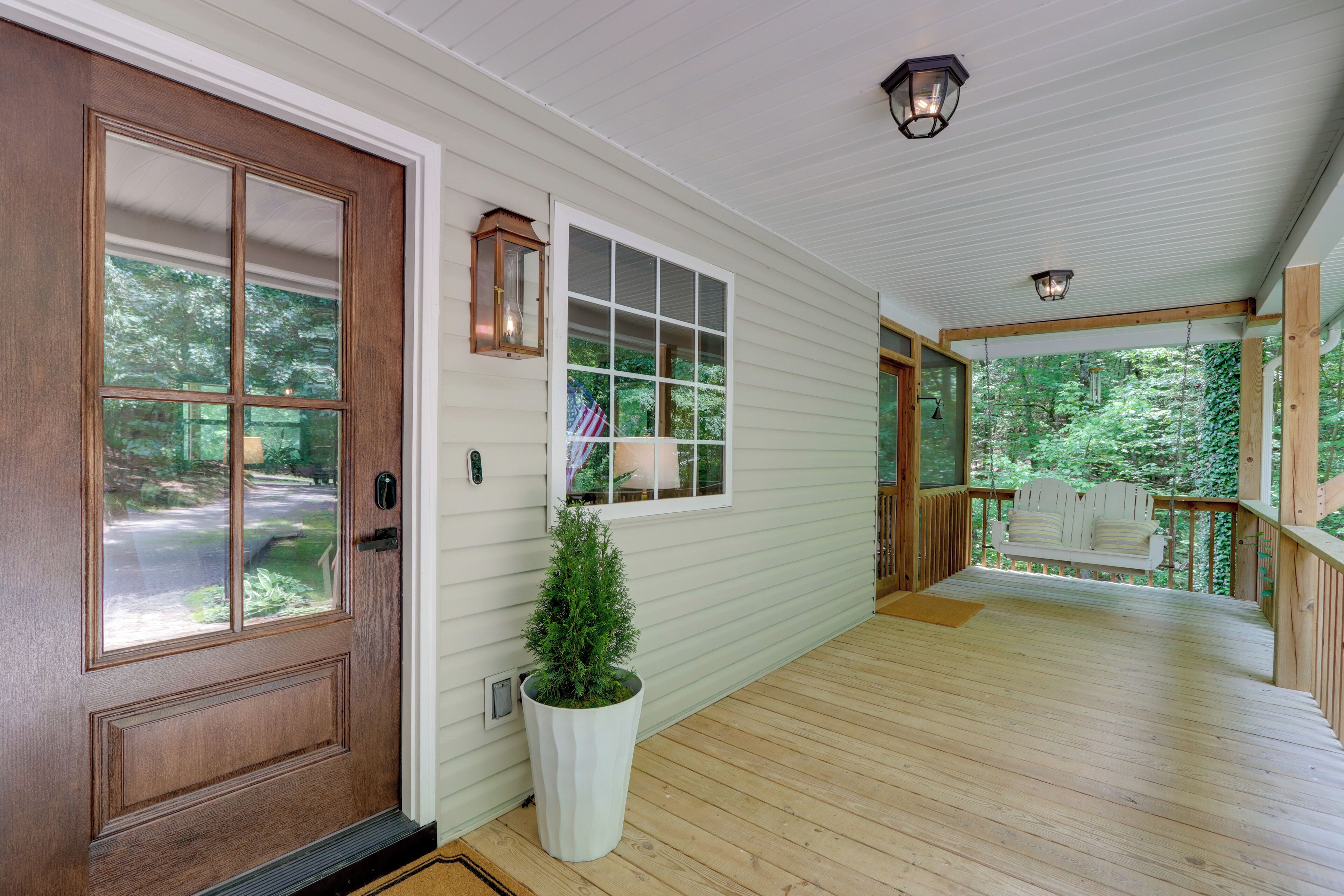 A wooden porch with a white door, a potted plant, and a bench.