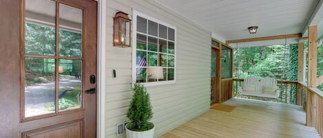 A wooden porch with a white door, a potted plant, and a bench.