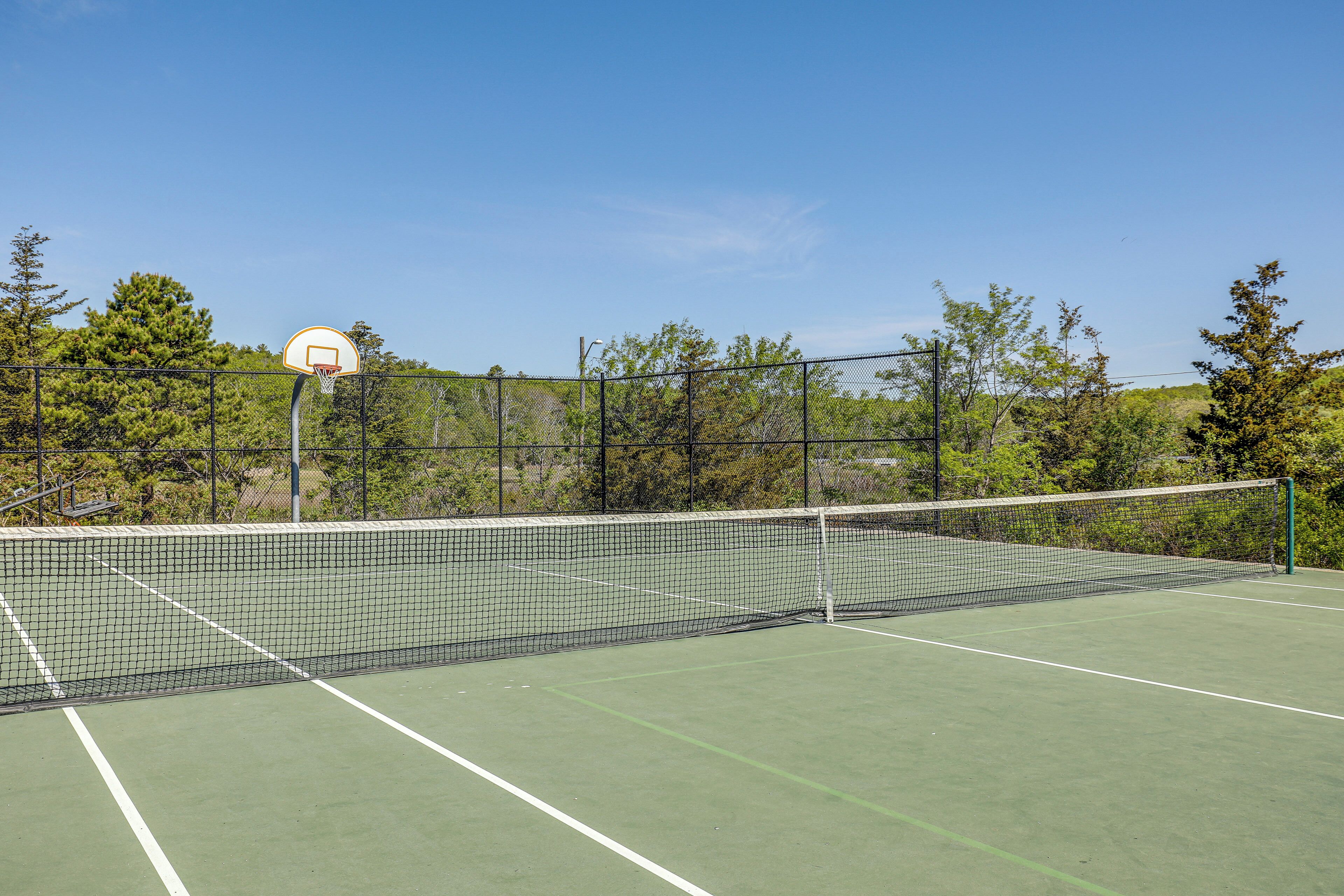 Un court de tennis avec un filet, entouré d’une clôture et d’arbres.