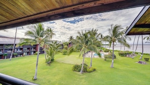 A view of a well-maintained lawn with palm trees, a pool, and a building with multiple balconies in the background. - Kaunakakai Vacation Rental w/ Pool Access & A/c! (Kaunakakai)
