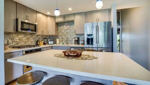 A modern kitchen with stainless steel appliances, a large island with stools, and pendant lighting. - Kaunakakai Vacation Rental w/ Pool Access & A/c! (Kaunakakai)