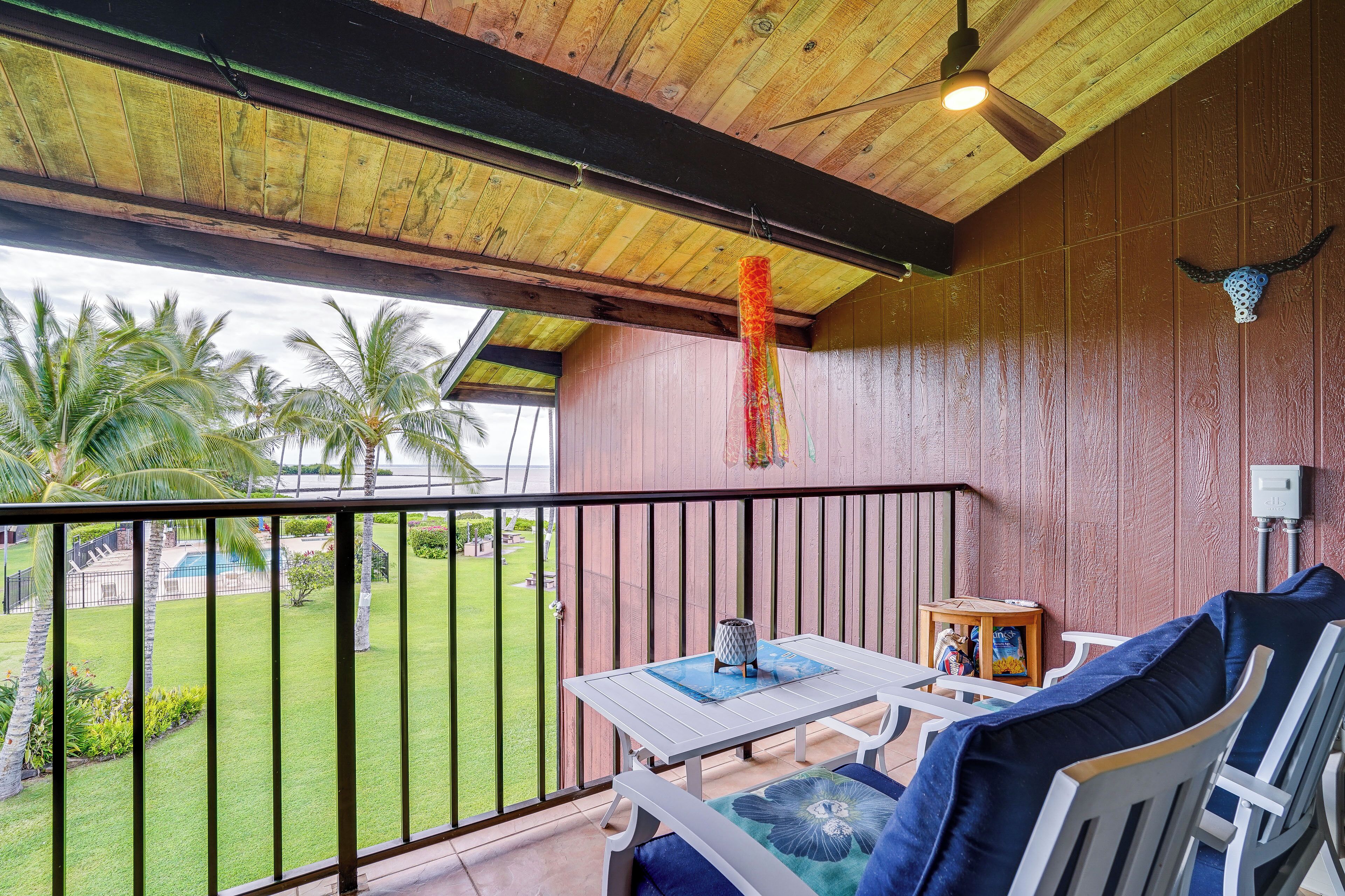Un balcon avec une table et des chaises, un ventilateur de plafond et une vue sur une piscine et des palmiers.