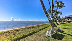 A bench on a grassy area with a view of the ocean and palm trees. - Kaunakakai Vacation Rental w/ Pool Access & A/c! (Kaunakakai)