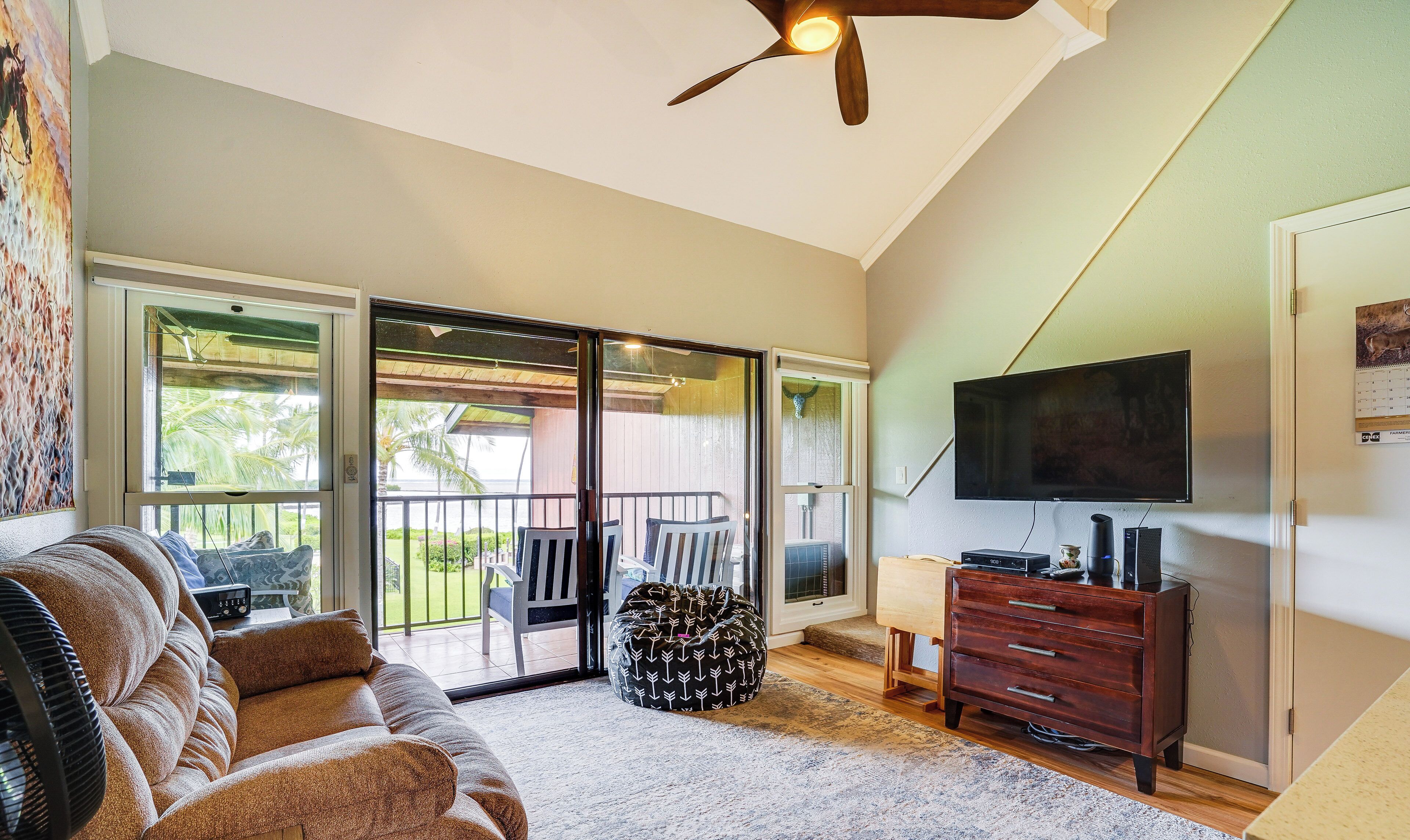 A living room with a sofa, a bean bag, a TV, and a ceiling fan.