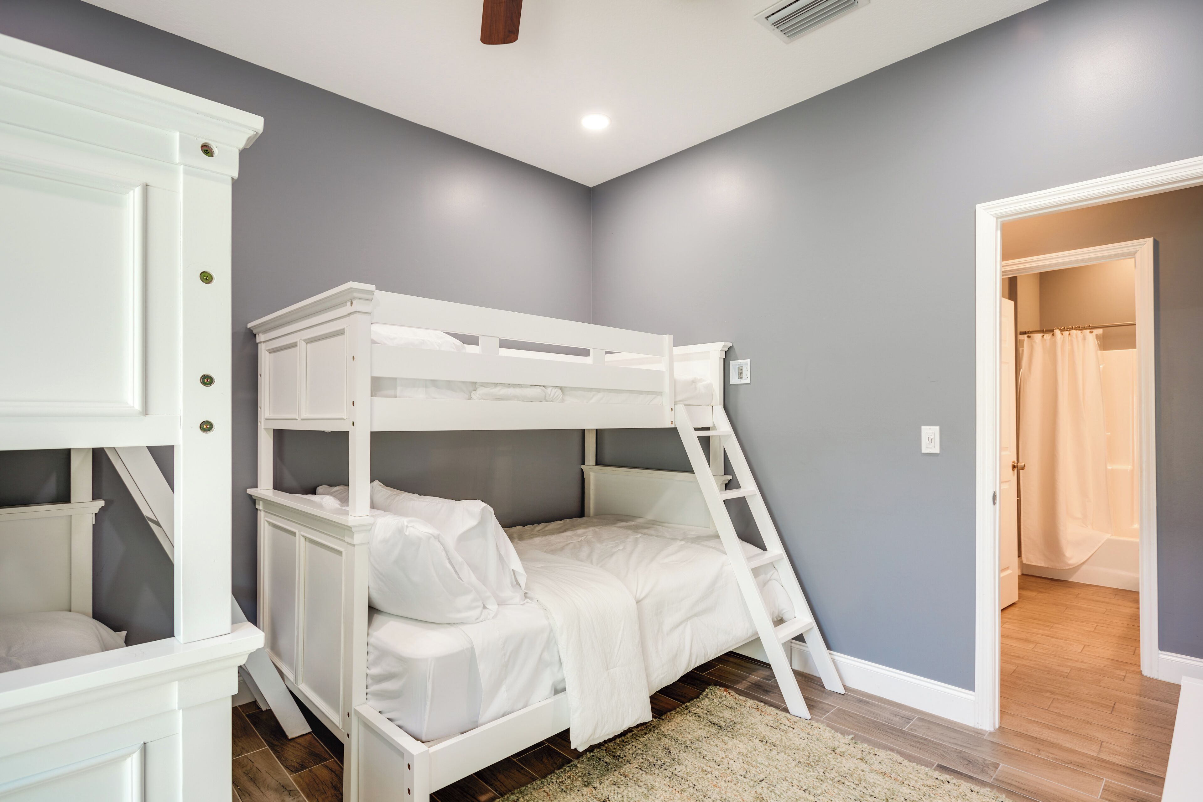 A bunk bed in a room with grey walls, wooden flooring, and white furniture.