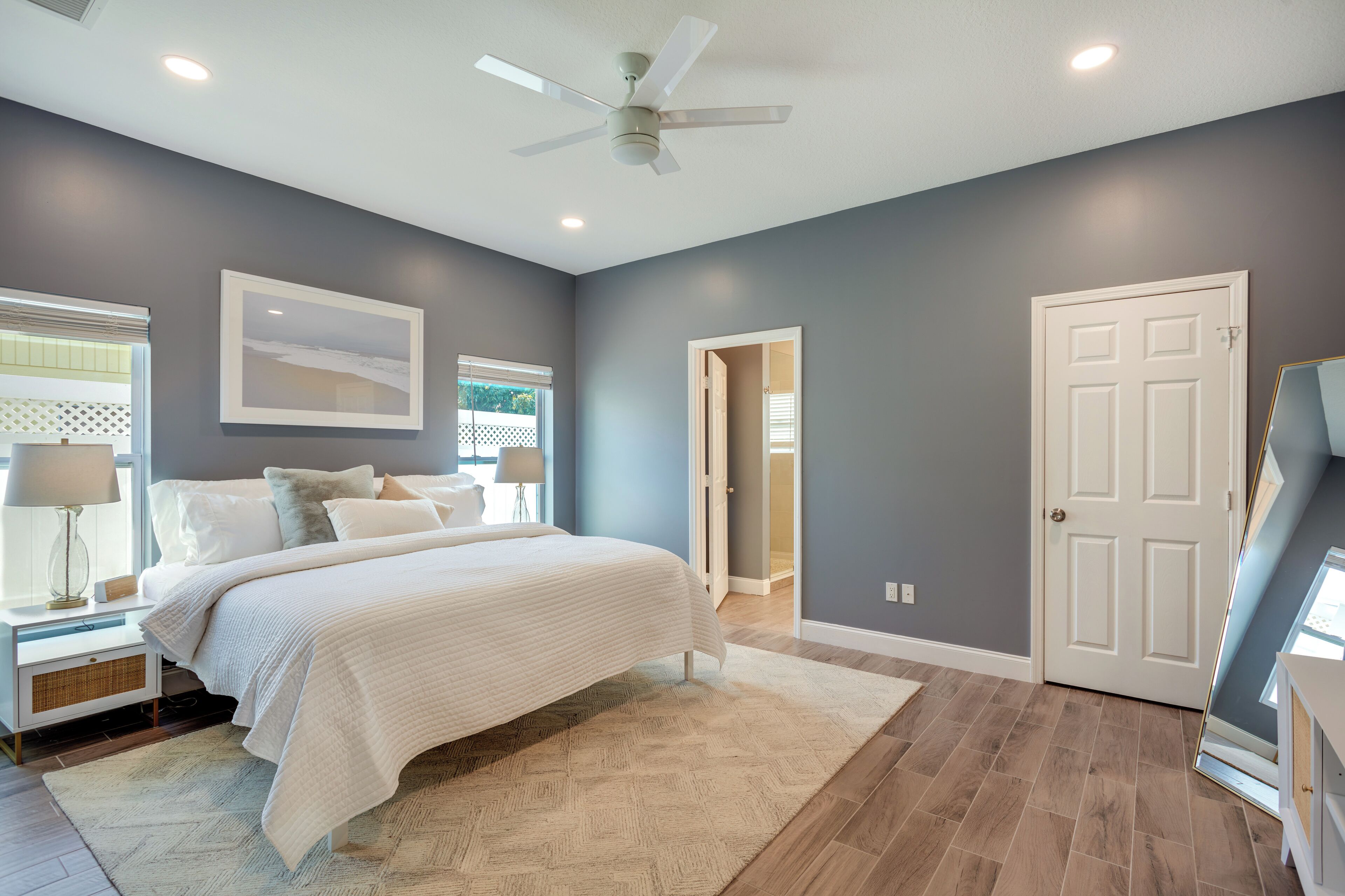 A bedroom with a bed, nightstands, a ceiling fan, and a door.