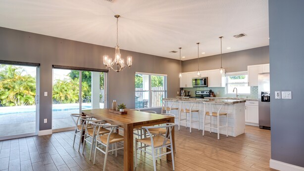 A spacious kitchen with a wooden dining table, white bar stools, and pendant lighting. - Florida Gem: Saltwater Pool By Beaches & Kayaking! (Jensen Beach)