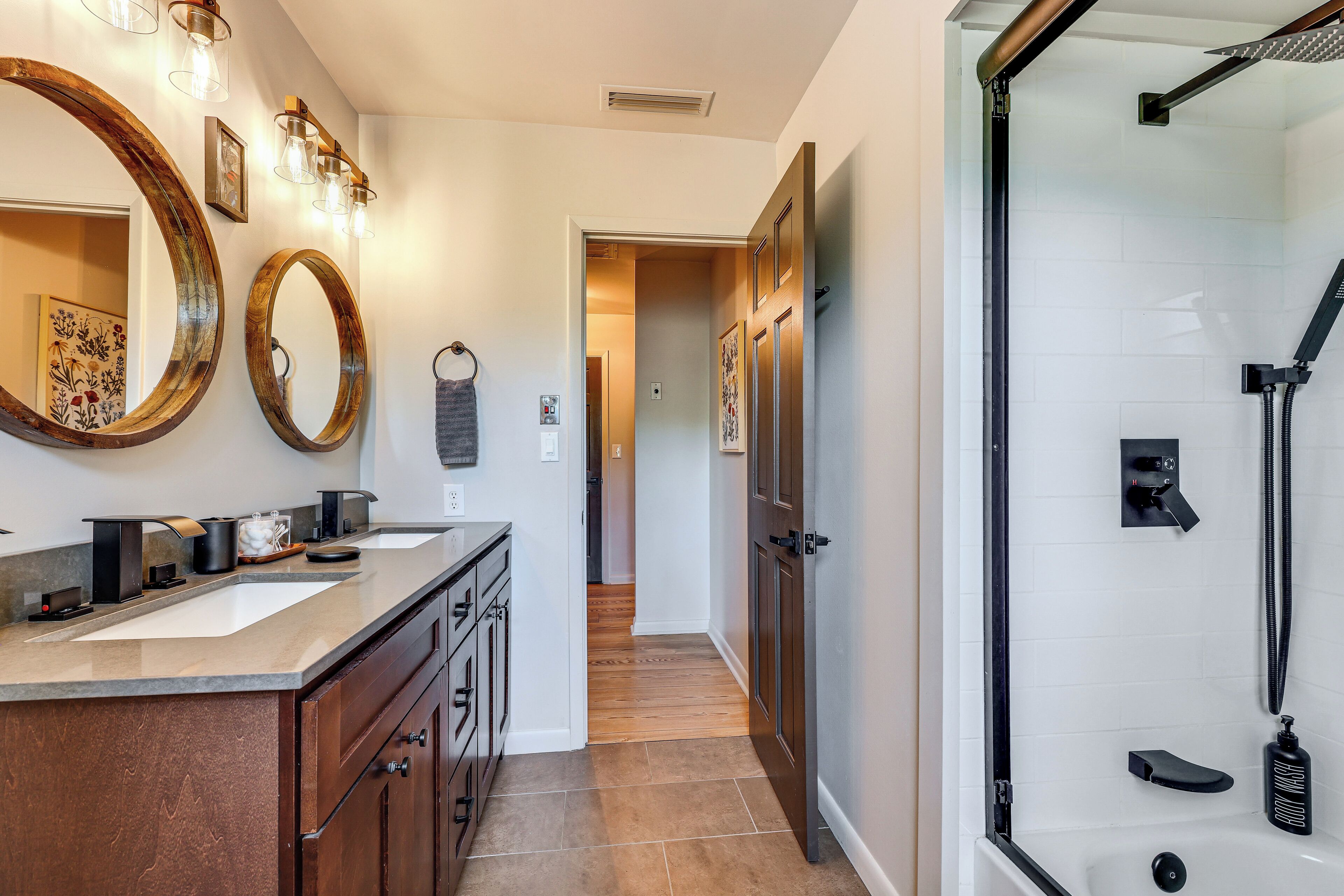 A modern bathroom with a large mirror, two sinks, and a walk-in shower.