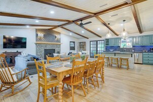 Un salón espacioso con una mesa de comedor, sillas de madera, una chimenea y una cocina con armarios verdes y una pared de acento de piedra.
