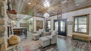A cozy living room with a fireplace, a dining area, and a large window with blinds. - Gorgeous Broken Bow Family Home w/ Private Hot Tub (Broken Bow)