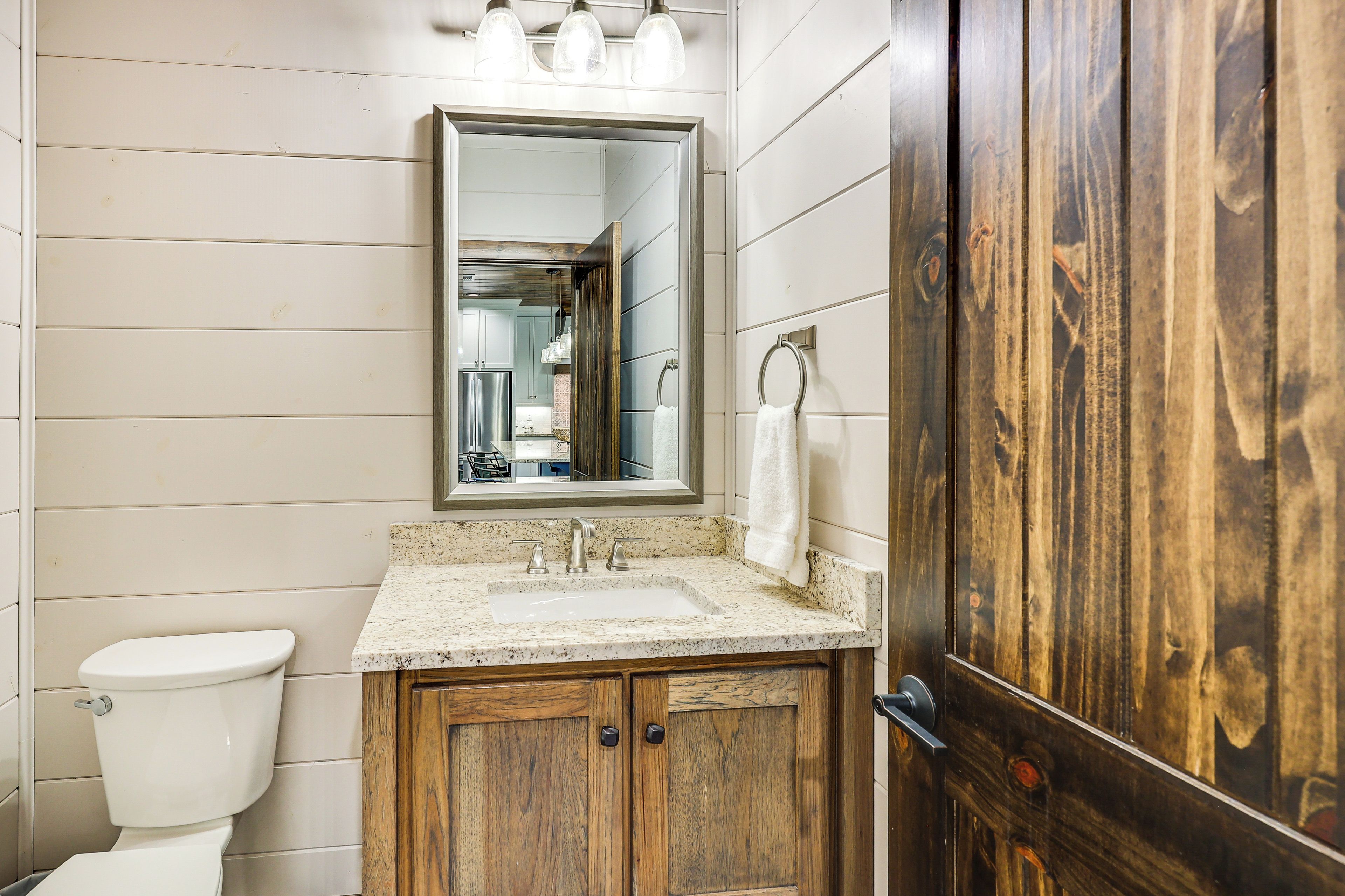 Une salle de bain avec un meuble-lavabo en bois, des toilettes blanches, un lavabo et un miroir au-dessus du meuble-lavabo.