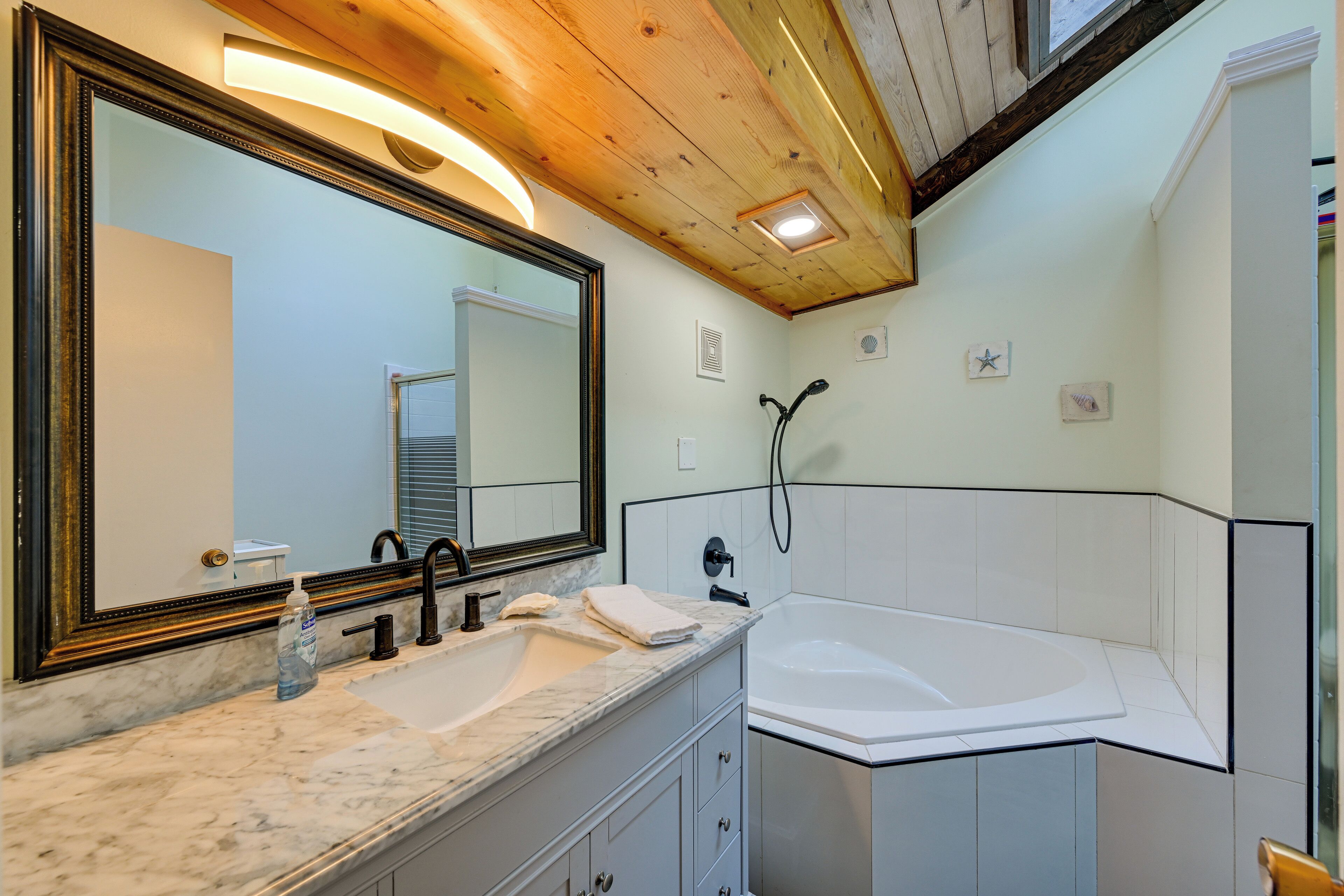 A bathroom with a large mirror, a sink, a bathtub, and a shower.