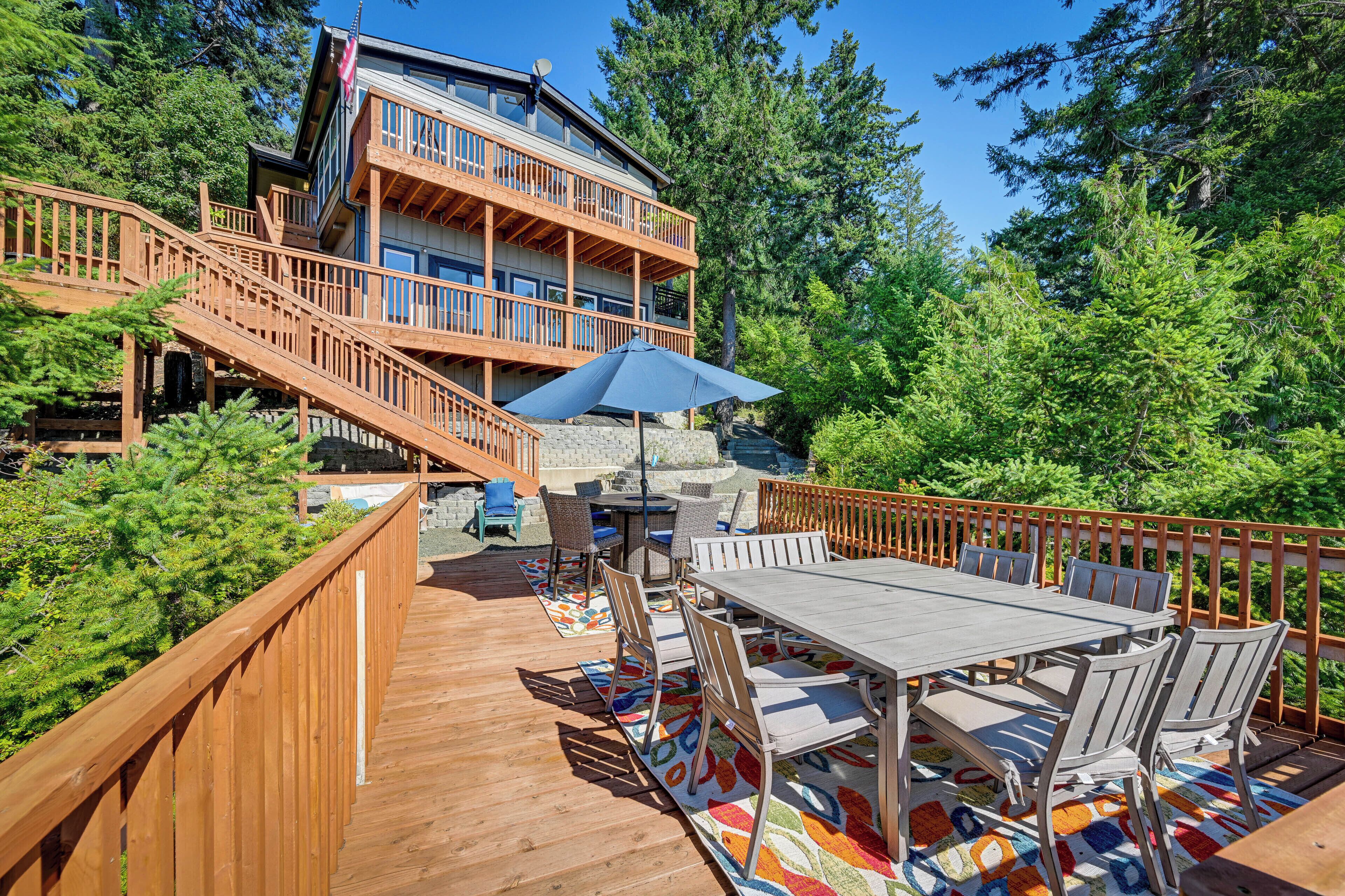 A multi-level wooden building with outdoor decks, a dining area with chairs and a table, and a view of surrounding trees.
