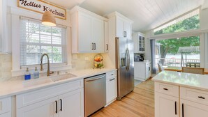 A modern kitchen with white cabinetry, a stainless steel refrigerator, and a window with blinds. - 'commodore Bay Waterfront Home on Lake Norman! (Mooresville)