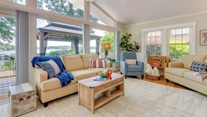 A spacious living room with a beige sofa, a wooden coffee table, and a blue armchair. A wooden chest of drawers and a wicker basket are also visible. - 'commodore Bay Waterfront Home on Lake Norman! (Mooresville)