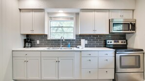 Una cocina moderna con armarios blancos, estufa de acero inoxidable, microondas y ventana sobre el fregadero.