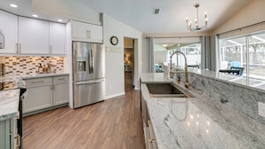 A modern kitchen with stainless steel appliances, a marble countertop, and a view of the outdoors through large windows. - Spring Hill Home w/ Private Pool & Games! (Spring Hill)