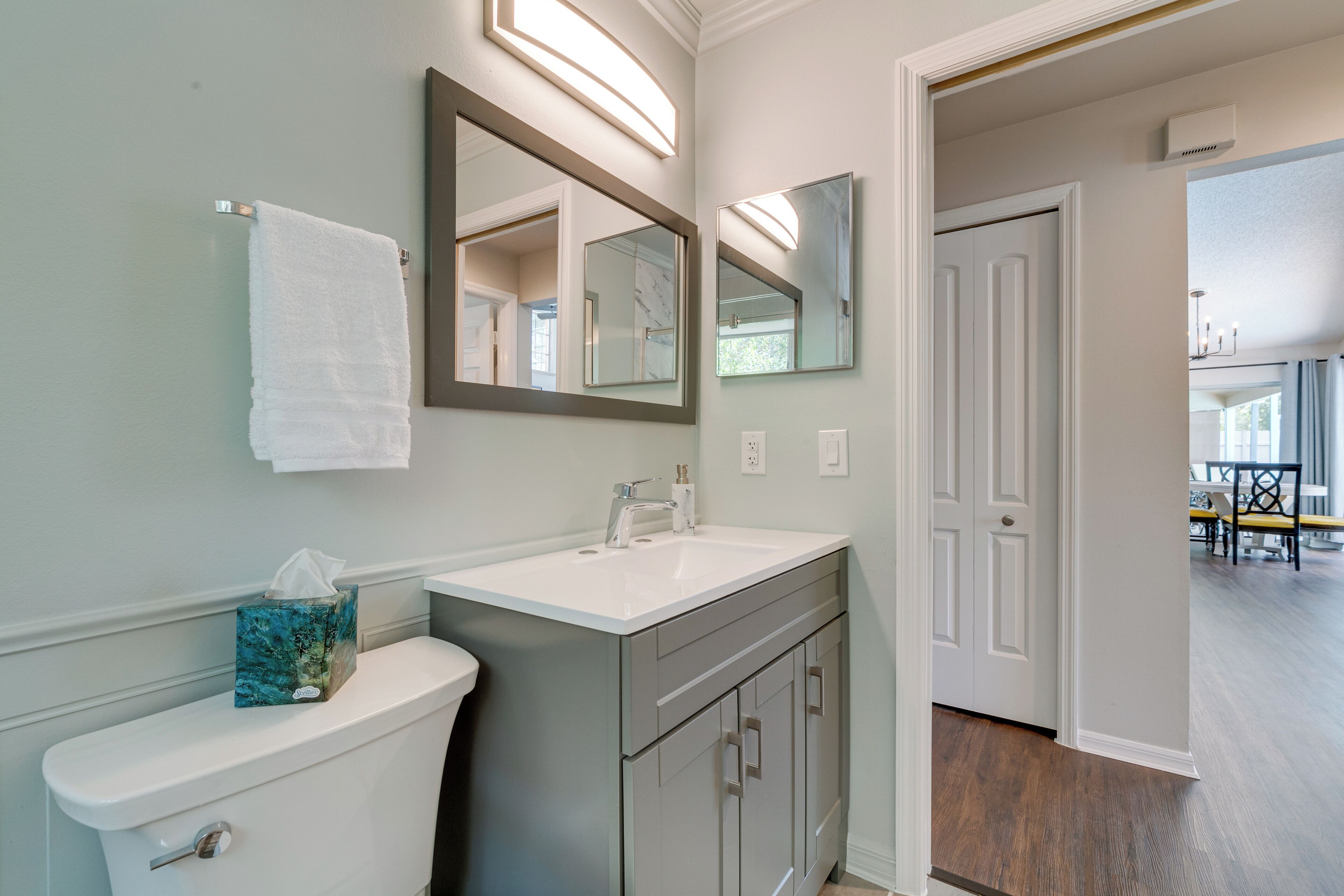 A bathroom with a toilet, sink, and cabinet. There is a towel hanging on the wall and a mirror above the sink.
