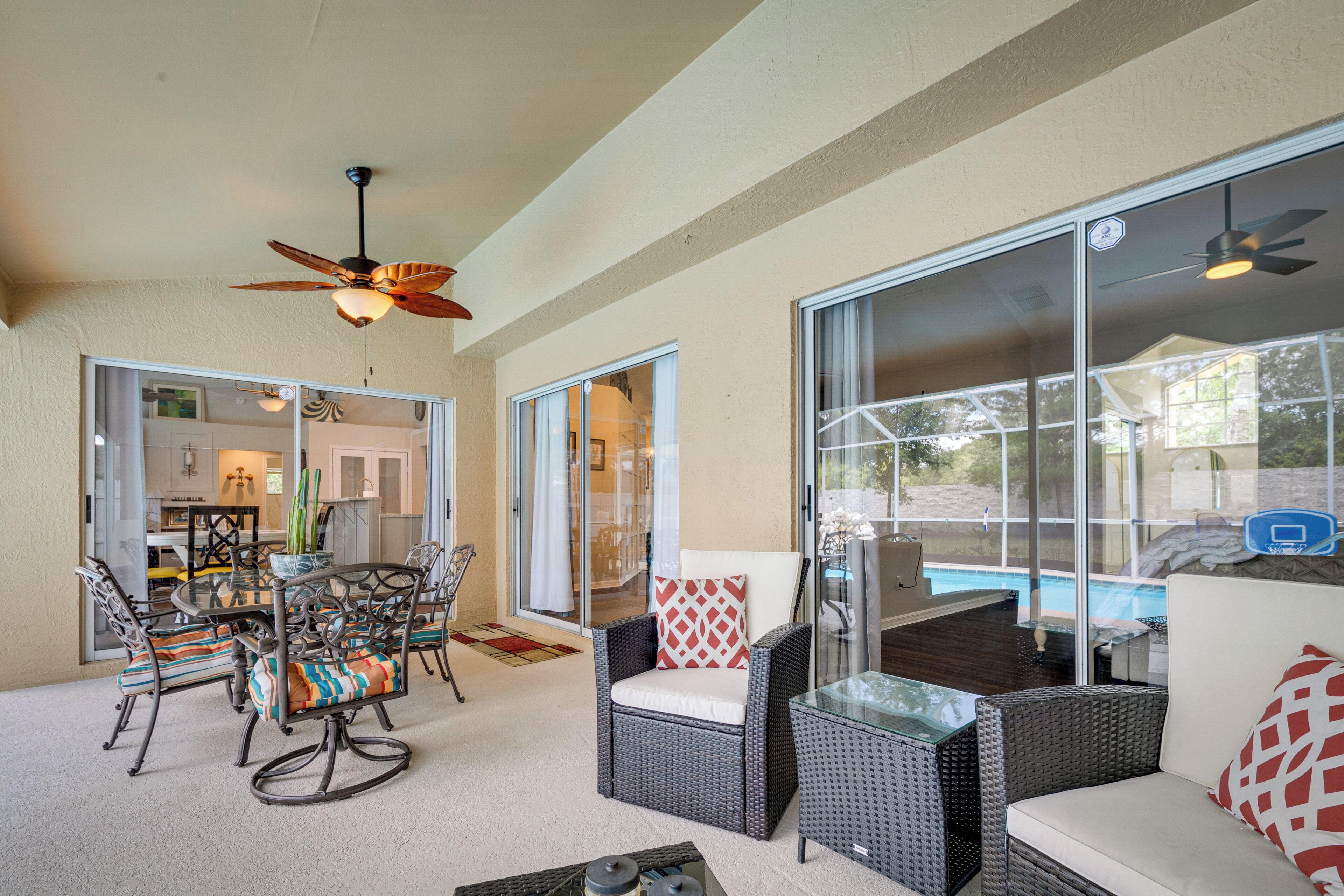 A covered patio area with wicker furniture, a glass table, and ceiling fans.