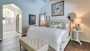 A bedroom with a large bed, a tufted bench, a ceiling fan, and a painting on the wall. - Spring Hill Home w/ Private Pool & Games! (Spring Hill)