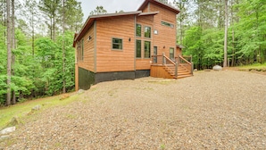 A wooden cabin with a gravel driveway, surrounded by trees.