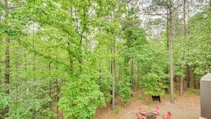 A forested area with a fire pit and red chairs.