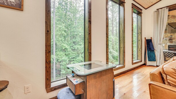 A room with a wooden desk, large windows, and a view of a forest.