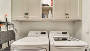 A laundry area with two white washing machines, a drying rack, and a cabinet above containing cleaning supplies.