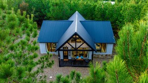 A house with a steeply pitched roof, large windows, and a porch with seating. - 'painted Sky' Modern Broken Bow Cabin w/ Hot Tub! (Broken Bow)