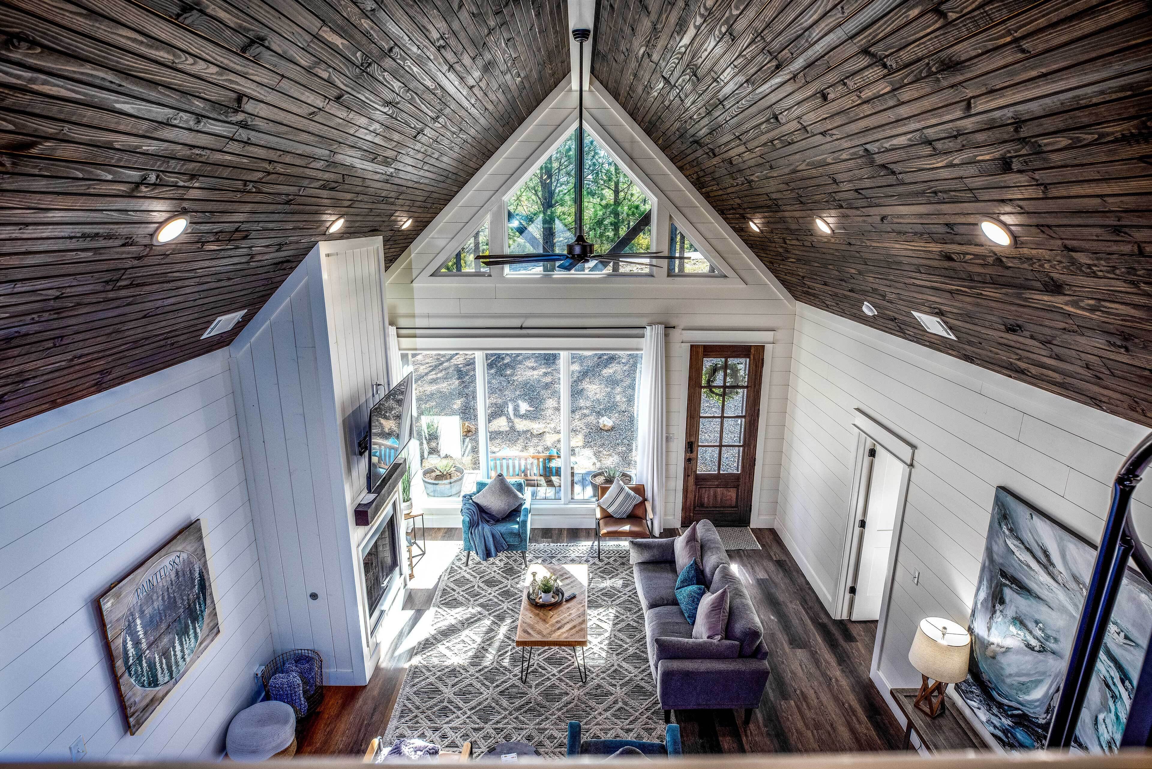 A spacious loft-style room with a high ceiling, wooden beams, and a large window offering a view of the outdoors.