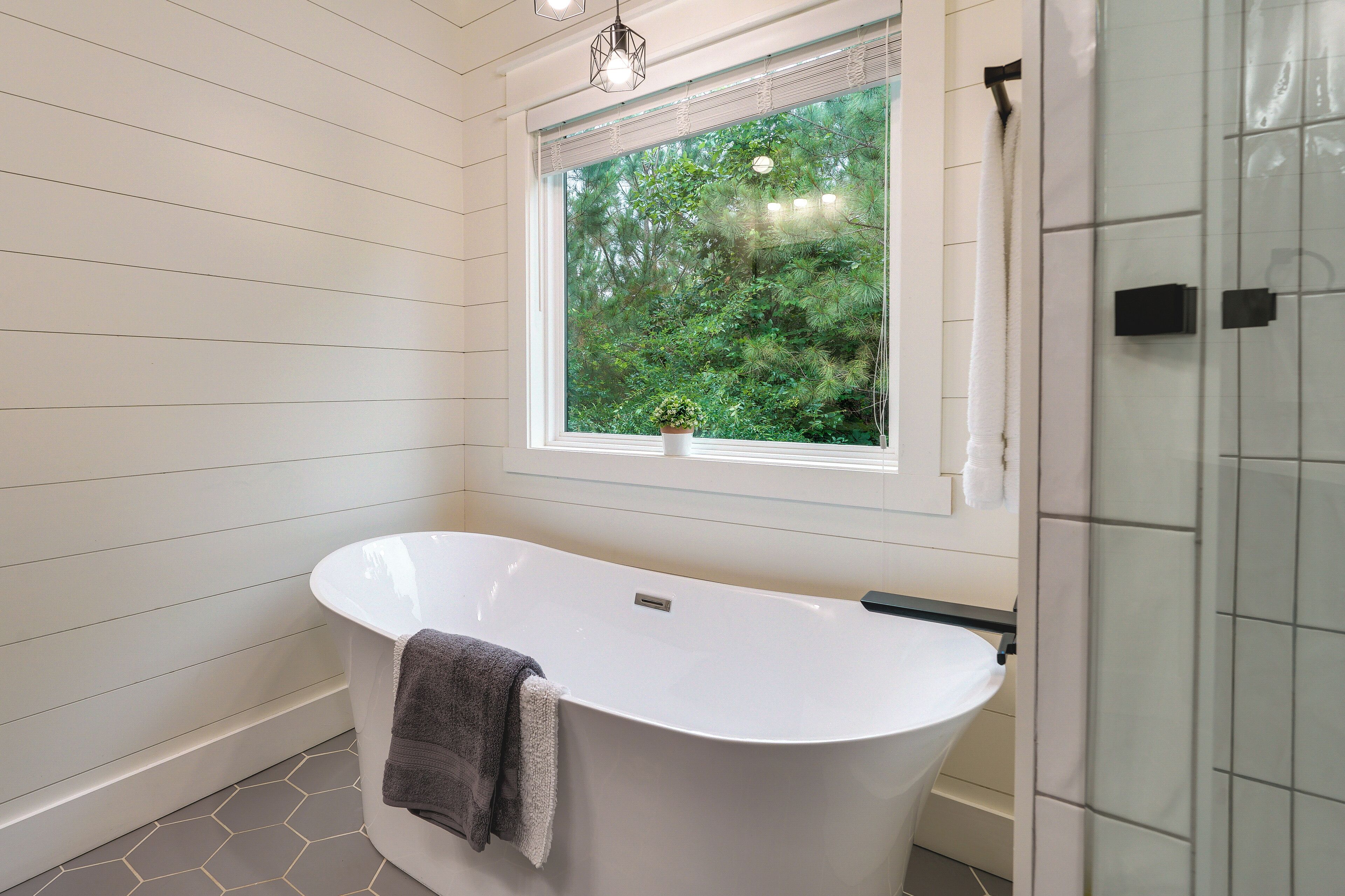 Une salle de bain moderne avec une baignoire sur pieds, une fenêtre donnant sur un paysage verdoyant et une plante en pot posée sur le rebord de la fenêtre.