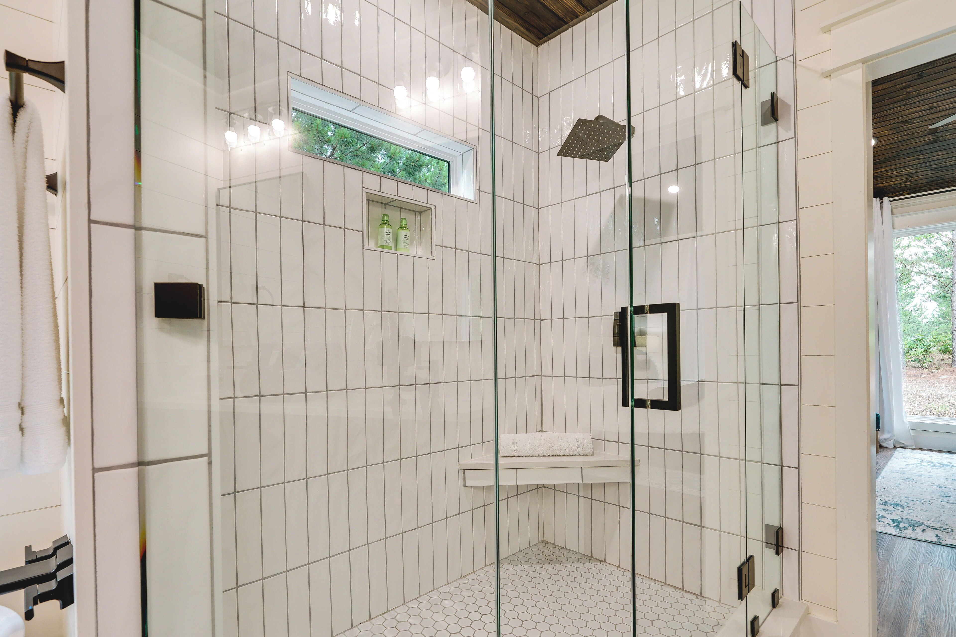 A modern bathroom with white subway tiles, a glass shower enclosure, a small window, and a white sink.