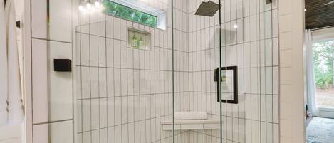 A modern bathroom with white subway tiles, a glass shower enclosure, a small window, and a white sink.