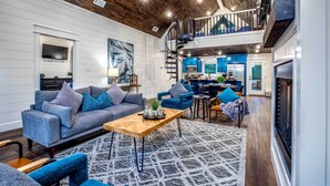 A spacious living area with a wooden ceiling, a sofa set, a coffee table, and a view of the kitchen and upper floor. - 'painted Sky' Modern Broken Bow Cabin w/ Hot Tub! (Broken Bow)