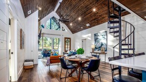 A spacious living area with a wooden ceiling, a dining table with chairs, and a spiral staircase. - 'painted Sky' Modern Broken Bow Cabin w/ Hot Tub! (Broken Bow)
