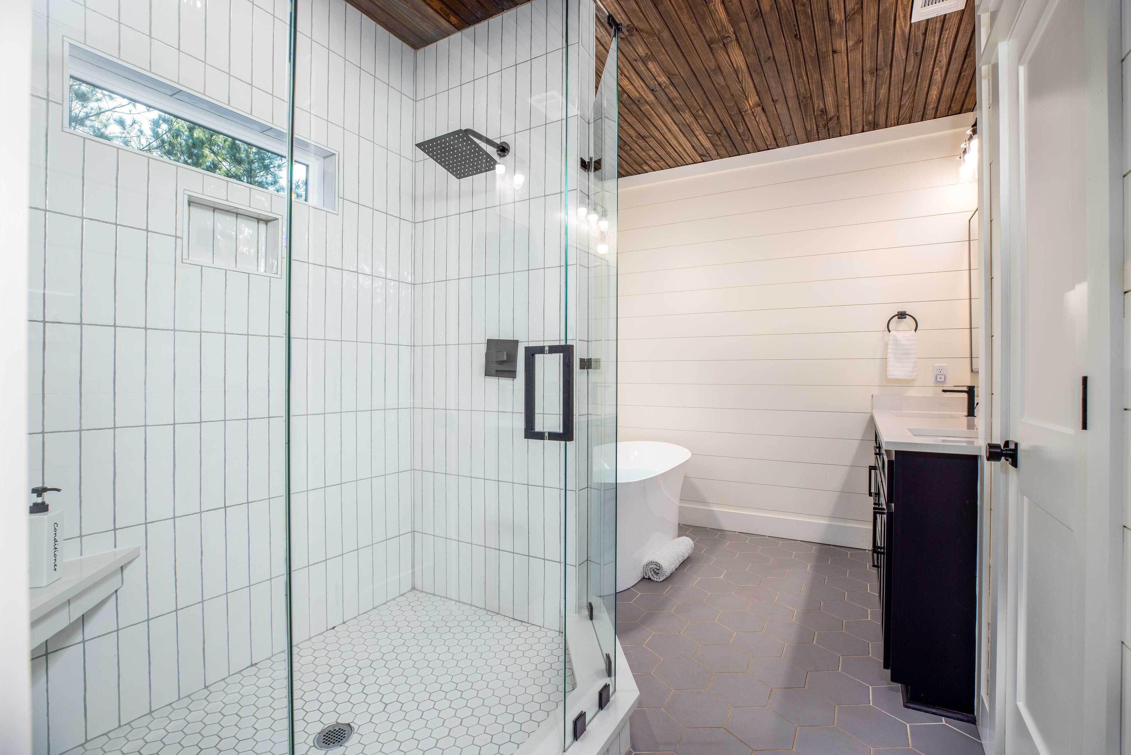 Un bagno moderno con doccia vetrata, pareti rivestite di piastrelle bianche, soffitto in legno e pavimento con motivo esagonale.