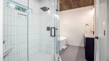 Un bagno moderno con doccia vetrata, pareti rivestite di piastrelle bianche, soffitto in legno e pavimento con motivo esagonale.