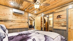 Una habitación tipo cabaña de madera con ventilador de techo, equipo de aire acondicionado y una cama con un estampado grande de lobo.