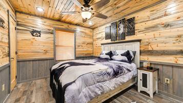 Un dormitorio con techo de madera, una cama con colcha de diseño blanco y negro, una mesita de noche con un reloj y una ventana con persianas.
