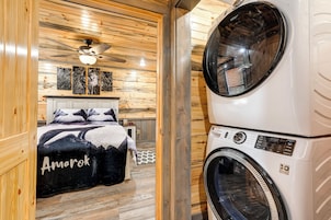 A laundry room with stacked washers and dryers, wooden walls, and a bed with a black and white blanket.