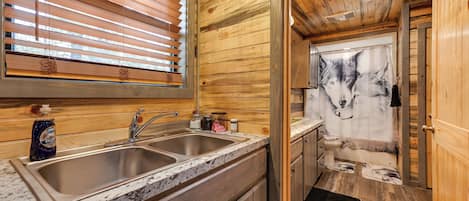 Un interior de madera con una zona de cocina que incluye un lavamanos doble y una ventana con persianas.