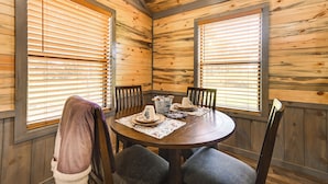 Una habitación con paneles de madera, con una mesa redonda dispuesta para cuatro personas, incluyendo una jarrón, un cuenco y un plato.